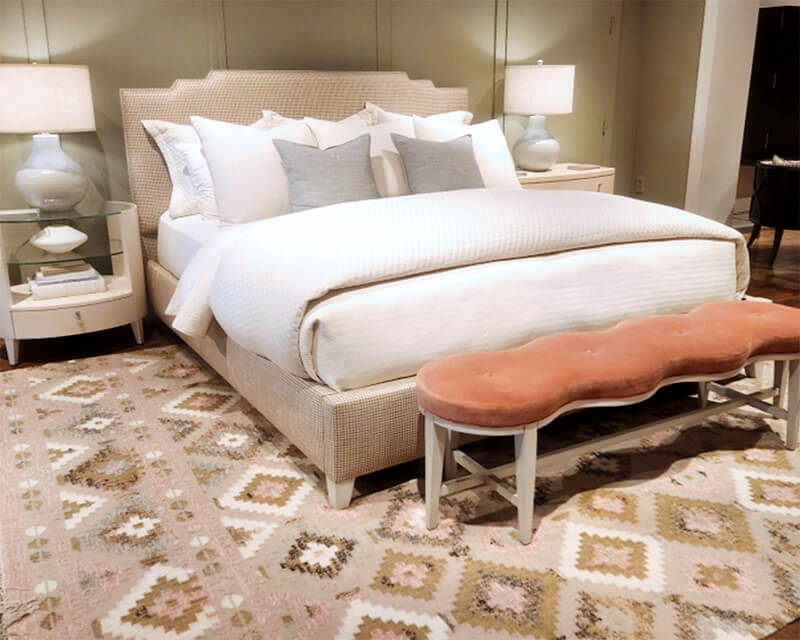 A bed, nightstands, and a bench on a rug with a geometric pattern in light greens and pinks